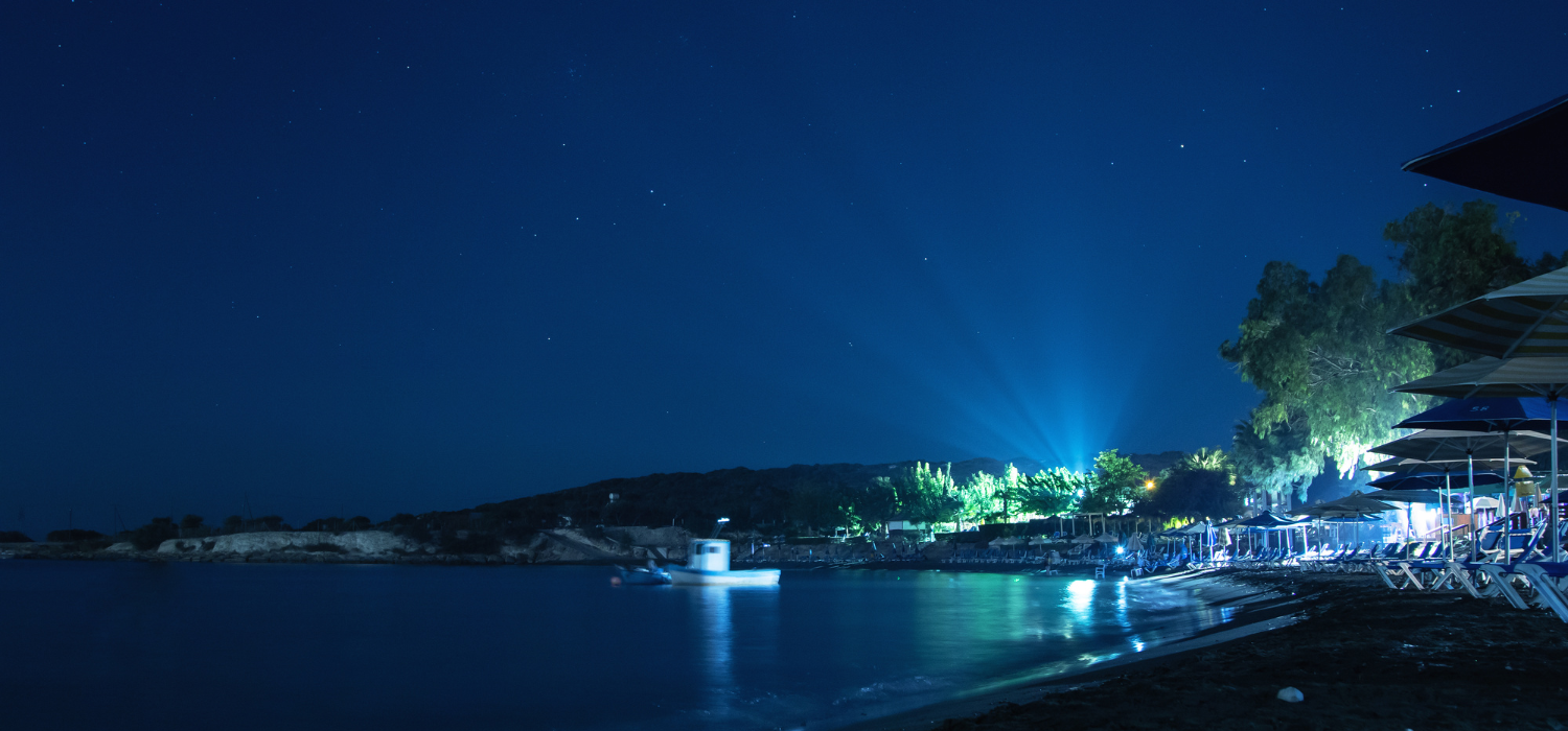 Coastal beach resort at night with rays of lights and sunbeds.